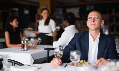 Wall Mural - Portrait of young thoughtful businessman resting and having dinner in cozy restaurant