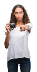 Sticker - Young hispanic woman taking pictures using vintage camera pointing with finger to the camera and to you, hand sign, positive and confident gesture from the front