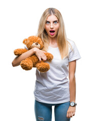 Canvas Print - Young beautiful blonde woman holding teddy bear over isolated background scared in shock with a surprise face, afraid and excited with fear expression