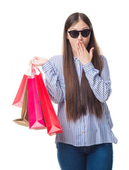 Wall Mural - Young Chinese woman over isolated background holding shopping bags on sales cover mouth with hand shocked with shame for mistake, expression of fear, scared in silence, secret concept