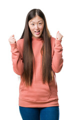 Wall Mural - Young Chinese woman over isolated background wearing sport sweathshirt celebrating surprised and amazed for success with arms raised and open eyes. Winner concept.