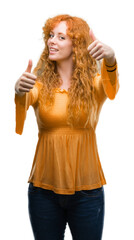 Wall Mural - Young redhead woman approving doing positive gesture with hand, thumbs up smiling and happy for success. Looking at the camera, winner gesture.