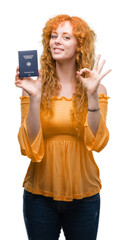 Sticker - Young redhead woman holding passport of Germany doing ok sign with fingers, excellent symbol