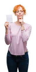 Sticker - Young redhead woman holding blank notebook serious face thinking about question, very confused idea