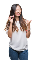 Canvas Print - Young asian woman eating pink macaron sweet over isolated background pointing and showing with thumb up to the side with happy face smiling