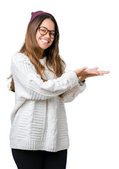 Canvas Print - Young beautiful brunette hipster woman wearing glasses and winter hat over isolated background Pointing to the side with hand and open palm, presenting ad smiling happy and confident