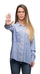 Sticker - Beautiful young woman wearing elegant shirt and glasses doing stop sing with palm of the hand. Warning expression with negative and serious gesture on the face.