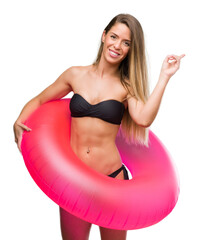 Sticker - Beautiful young woman in bikini holding pink float very happy pointing with hand and finger to the side