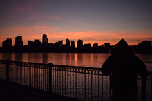 Silhouette Of Person Looking Over City  Across Body Of Water At Sunset