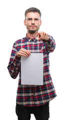 Sticker - Young hipster adult man holding blank paper sheet pointing with finger to the camera and to you, hand sign, positive and confident gesture from the front