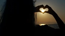 Silhouette Of Teen With Love Gesture. A View Of Girl Silhouette Showing The Love Heart Gesture Against Bright Sun During Nightfall.
