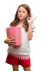 Wall Mural - Brunette hispanic girl eating popcorn doing ok sign with fingers, excellent symbol