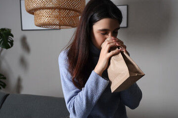 Wall Mural - Young woman with paper bag having panic attack at home