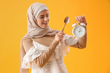 Wall Mural - Muslim woman with spoon and alarm clock on yellow background