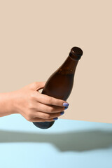 Female hand with bottle of cold beer on color background