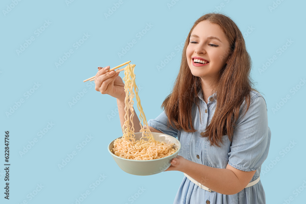 Young woman eating Chinese noodles on blue background