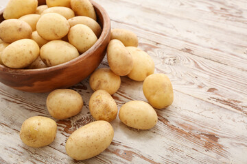 Bowl with raw potatoes on white wooden background