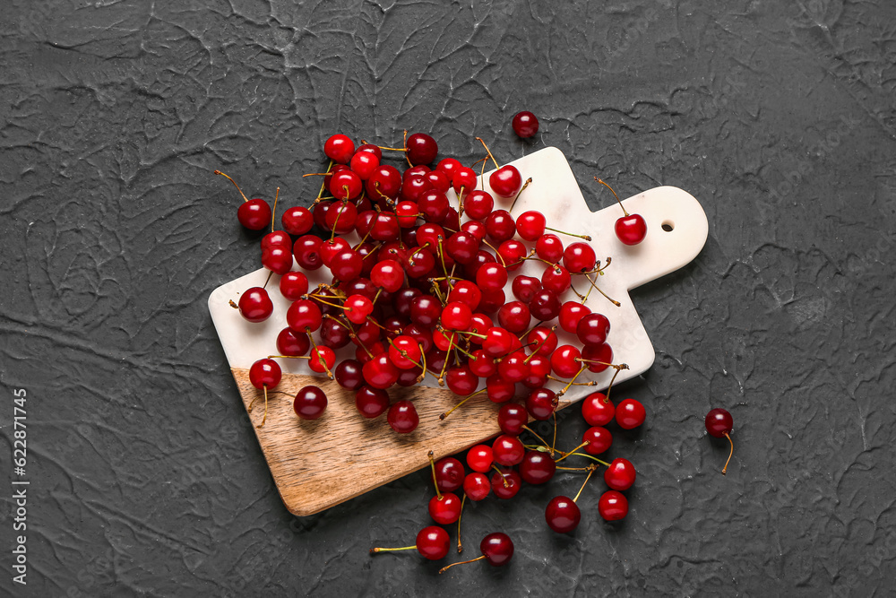 Board with red sweet cherries on black background