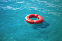 Red Lifebuoy Ring On Blue Shiny Water Surface Texture, Red Swimming Pool Ring Float In Blue Water Lost At Sea In Summer Safety Equipment, Rescue Buoy Floating On Sea To Rescue People From Drowning Man