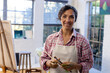 © Wavebreak Media - Portrait of happy biracial woman wearing apron holding brushes in home studio