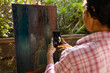 © Wavebreak Media - Biracial woman wearing apron using smartphone for taking picture of painting on easel in garden