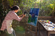 © Wavebreak Media - Biracial woman wearing apron using smartphone for taking picture of painting on easel in garden