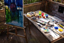 Close Up Of Easel With Painting And Table With Painting Equipment On Terrace
