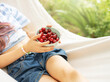 A little girl rests in a hammock and eats cherries in the summer.