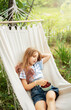 A little girl rests in a hammock and eats cherries in the summer.