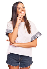 Wall Mural - Young hispanic woman wearing casual clothes looking confident at the camera with smile with crossed arms and hand raised on chin. thinking positive.