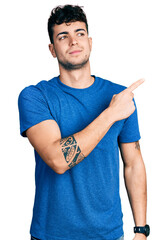 Canvas Print - Young hispanic man wearing casual t shirt pointing with hand finger to the side showing advertisement, serious and calm face