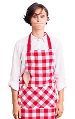 Sticker - Beautiful young woman with short hair wearing professional cook apron puffing cheeks with funny face. mouth inflated with air, crazy expression.