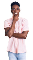 Sticker - Young african american man wearing casual clothes looking confident at the camera smiling with crossed arms and hand raised on chin. thinking positive.