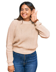 Poster - Young latin girl wearing wool winter sweater smiling with hand over ear listening an hearing to rumor or gossip. deafness concept.