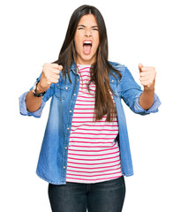 Poster - Young brunette woman wearing casual clothes angry and mad raising fists frustrated and furious while shouting with anger. rage and aggressive concept.