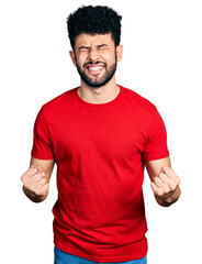 Wall Mural - Young arab man with beard wearing casual red t shirt very happy and excited doing winner gesture with arms raised, smiling and screaming for success. celebration concept.