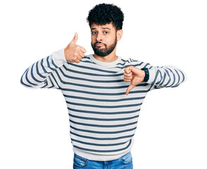 Wall Mural - Young arab man with beard wearing casual striped sweater doing thumbs up and down, disagreement and agreement expression. crazy conflict