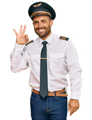 Handsome man with beard wearing airplane pilot uniform smiling positive doing ok sign with hand and fingers. successful expression.