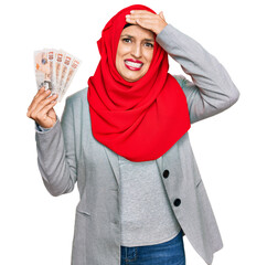 Canvas Print - Beautiful hispanic woman wearing islamic hijab holding 10 pounds banknotes stressed and frustrated with hand on head, surprised and angry face