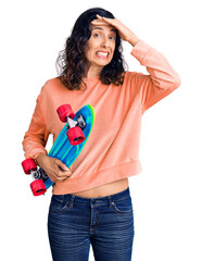 Wall Mural - Young beautiful hispanic woman holding skate stressed and frustrated with hand on head, surprised and angry face