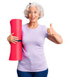 © Krakenimages.com - Senior grey-haired woman holding yoga mat smiling happy and positive, thumb up doing excellent and approval sign