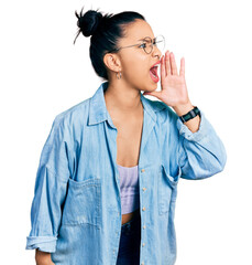 Wall Mural - Beautiful hispanic woman wearing casual denim jacket and glasses shouting and screaming loud to side with hand on mouth. communication concept.