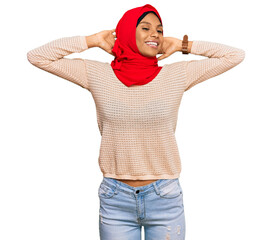 Wall Mural - Young african american woman wearing traditional islamic hijab scarf relaxing and stretching, arms and hands behind head and neck smiling happy