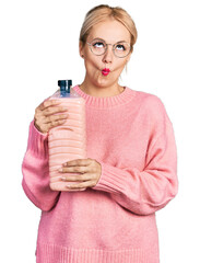 Canvas Print - Young blonde woman holding detergent bottle making fish face with mouth and squinting eyes, crazy and comical.