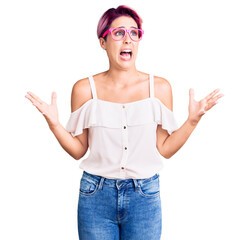 Canvas Print - Young beautiful woman with pink hair wearing casual clothes and glasses crazy and mad shouting and yelling with aggressive expression and arms raised. frustration concept.