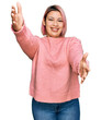 © Krakenimages.com - Hispanic woman with pink hair wearing casual winter sweater looking at the camera smiling with open arms for hug. cheerful expression embracing happiness.