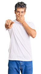 Wall Mural - Young handsome man wearing casual white tshirt laughing at you, pointing finger to the camera with hand over mouth, shame expression