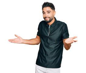 Canvas Print - Young man with beard wearing sportswear clueless and confused expression with arms and hands raised. doubt concept.