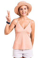 Poster - Young blonde woman wearing summer hat smiling looking to the camera showing fingers doing victory sign. number two.