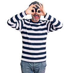 Poster - Middle age handsome man wearing burglar mask doing ok gesture like binoculars sticking tongue out, eyes looking through fingers. crazy expression.